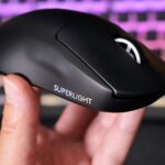 A hand holds up a jet black sculpted plastic mouse with a white scroll wheel and white words “Superlight” printed on the side.