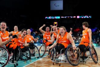 A Dutch wheelchair basketball team in orange jerseys cheers on the basketball court