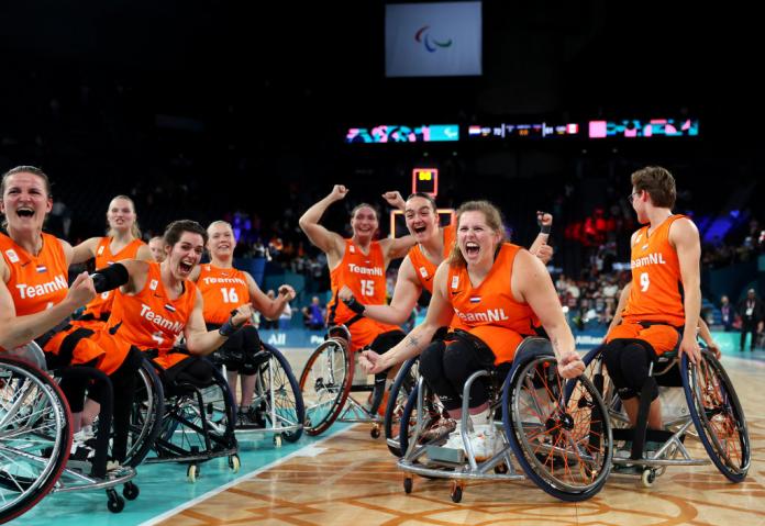 A Dutch wheelchair basketball team in orange jerseys cheers on the basketball court